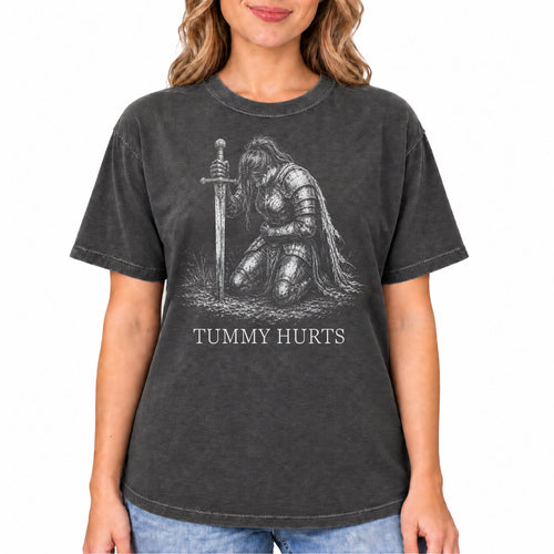 A woman wearing a dark gray washed graphic t-shirt with a sketch of a kneeling armored figure next to a sword and the text 'TUMY HURTS'.