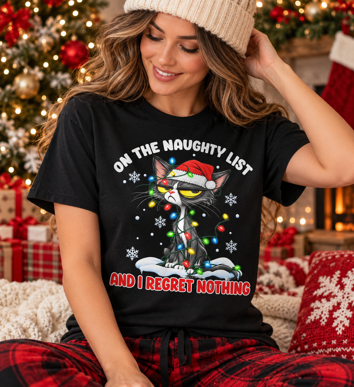 A black short-sleeve t-shirt with a graphic of a grumpy cat wearing a Santa hat and Christmas lights, with the text 'ON THE NAUGHTY LIST' and 'AND I REGRET NOTHING' on a white background.