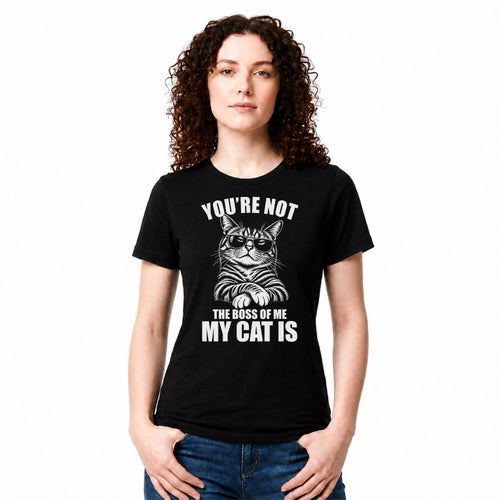 A woman with curly brown hair wearing a black short-sleeve graphic t-shirt with a white cat illustration and the text 'YOU'RE NOT THE BOSS OF ME MY CAT IS'. She is also wearing blue jeans, standing against a plain white background.