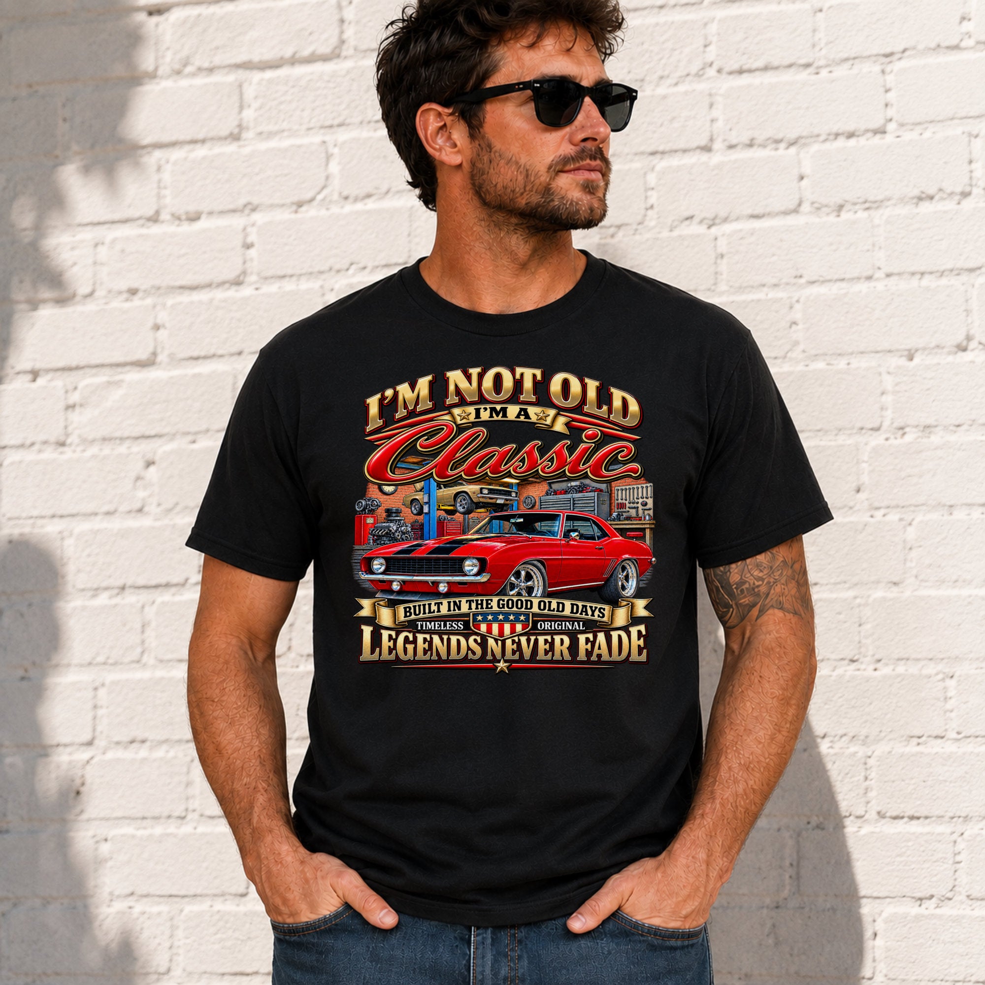 A man wearing a black graphic t-shirt with a red muscle car design and text, standing against a white brick wall.