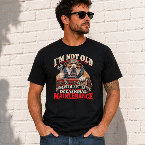 A man wearing a black graphic t-shirt with a bulldog and mechanic design, standing against a white brick wall.