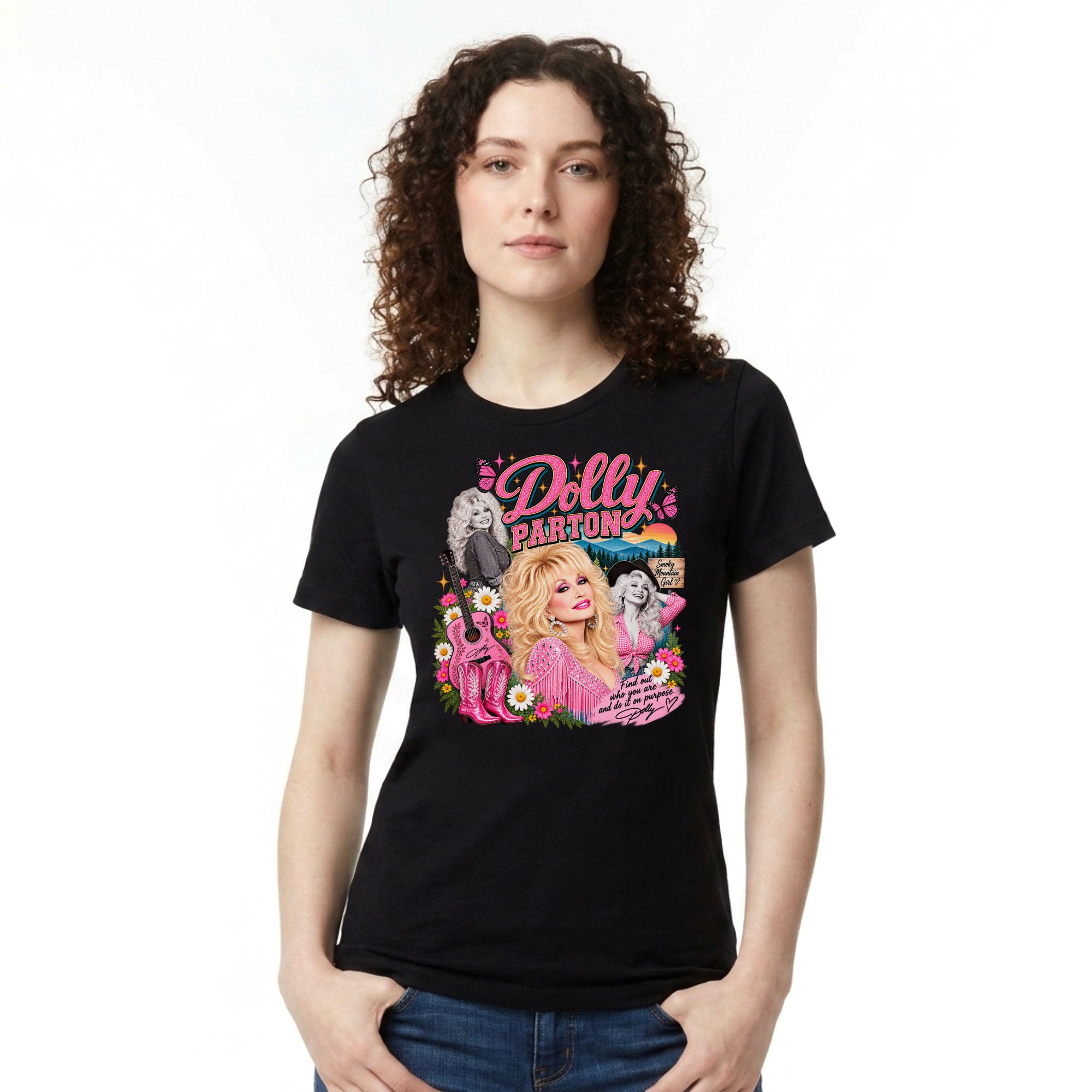 A woman with curly brown hair wearing a black short-sleeve graphic t-shirt featuring a colorful 'Dolly Parton' print, paired with blue jeans, against a plain white background.