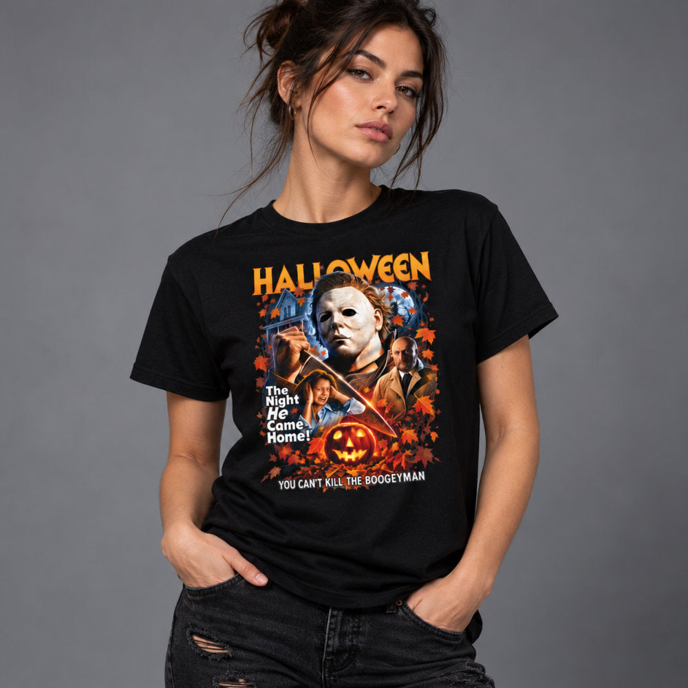 A woman modeling a black graphic t-shirt featuring Michael Myers from the Halloween movie franchise. The shirt has a colorful front print with the word 'HALLOWEEN' in orange, Michael Myers' mask, a pumpkin, and text reading 'The Night He Came Home!' and 'YOU CAN'T KILL THE BOOGEYMAN'.