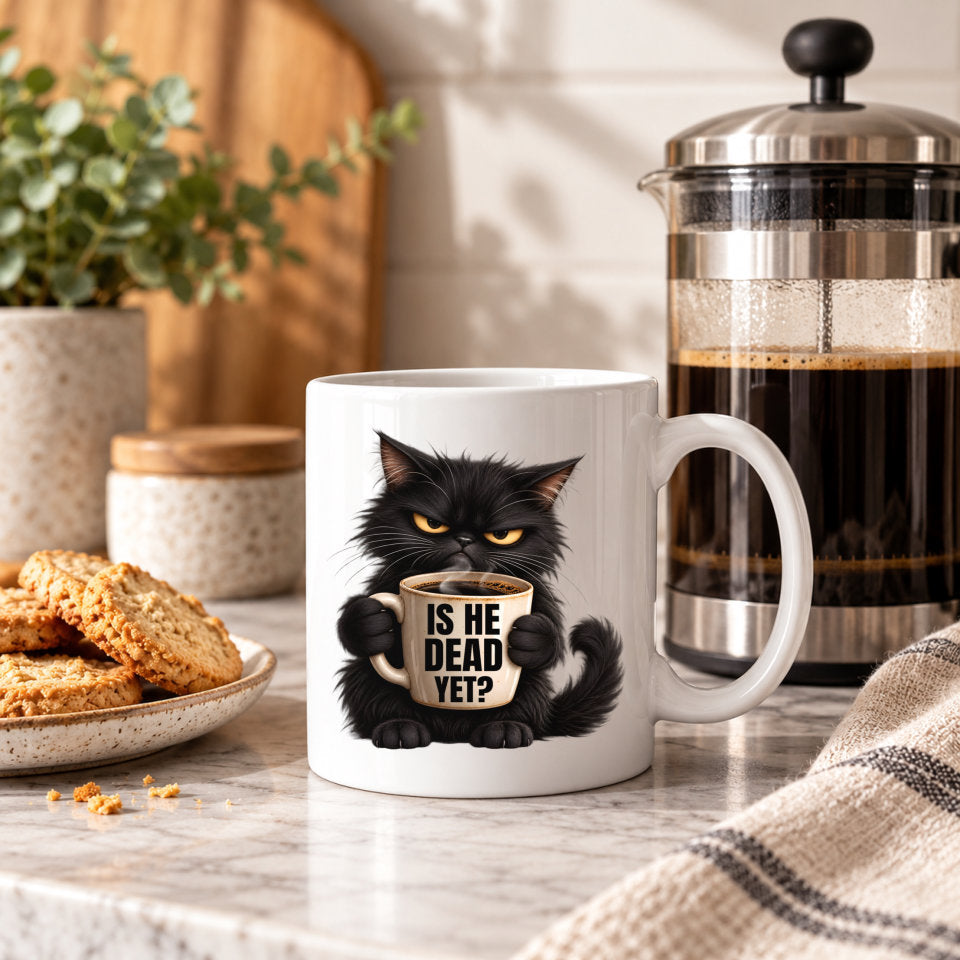 A white ceramic coffee mug featuring a black cat holding a cup with the text 'IS HE DEAD YET?' in a cozy kitchen setting next to a French press and cookies.