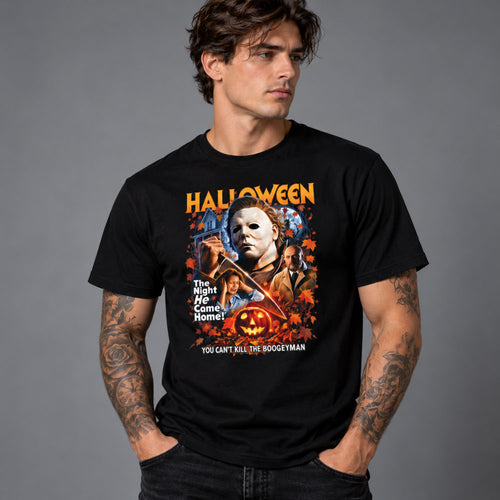 A man wearing a black graphic t-shirt featuring a Halloween-themed print with Michael Myers, a pumpkin, and the text 'HALLOWEEN' and 'YOU CAN'T KILL THE BOODLEYMAN', set against a solid gray studio background.