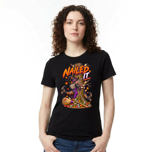 A woman with curly brown hair wearing a black short-sleeve graphic t-shirt with a 'Nailed It' witch tree illustration, paired with blue jeans, against a plain white background.