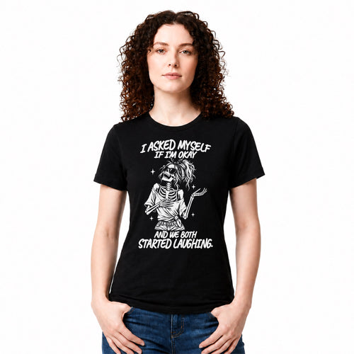A woman with curly brown hair wearing a black graphic t-shirt and blue jeans, standing against a plain white background. The t-shirt features a white graphic of a skeleton holding a guitar with the text 'I ASKED MYSELF IF I'M OKAY AND WE BOTH STARTED LAUGHING'.