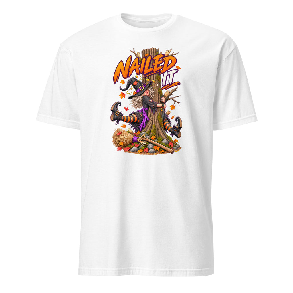 A white short-sleeve crewneck t-shirt featuring a colorful graphic print of a witch with a broomstick nailed to a tree trunk, with the text 'NAIL IT' in orange above.