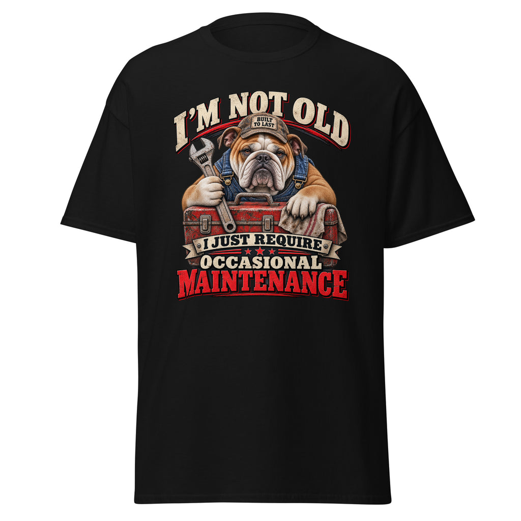 A black short-sleeve crewneck t-shirt featuring a graphic of an bulldog wearing a mechanic's hat and holding a wrench and toolbox, with the text 'I'M NOT OLD I JUST REQUIRE OCCASIONAL MAINTENANCE' in red, white, and beige.