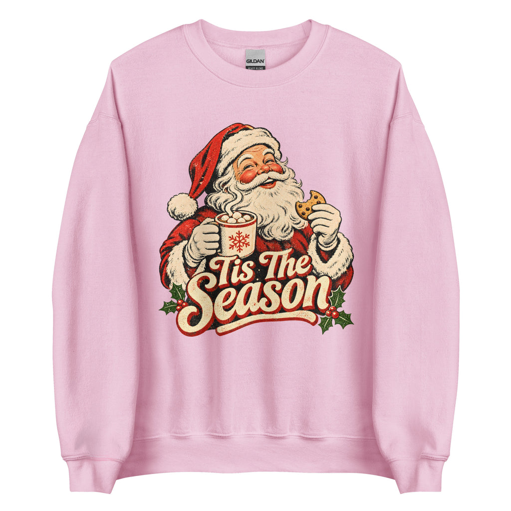 A light pink crewneck sweatshirt featuring a vintage-style graphic of Santa Claus holding a mug with the text 'Tis The Season' in red and cream lettering.